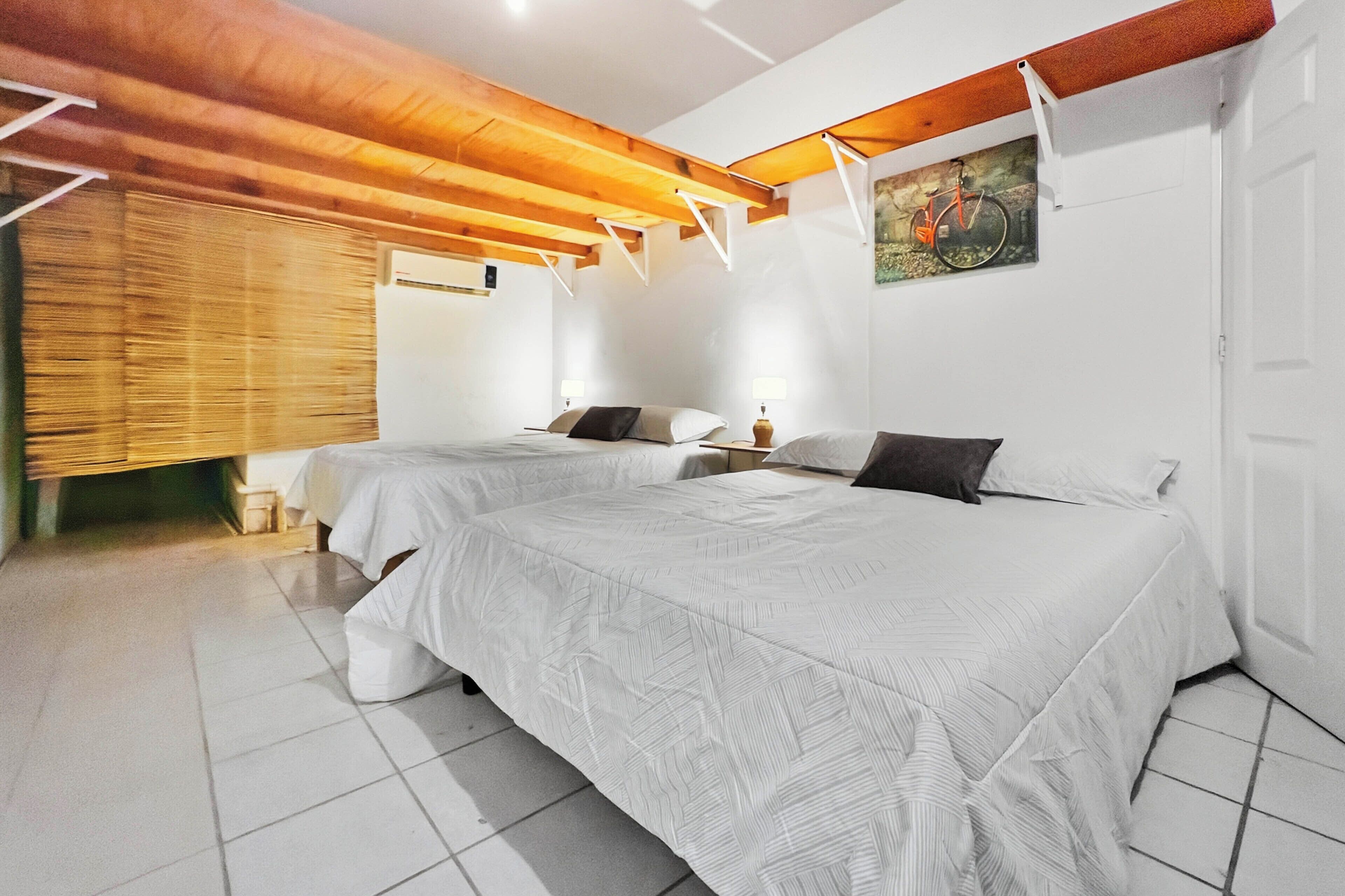 A hotel room with two beds, wooden ceiling beams, white walls, and a tiled floor.