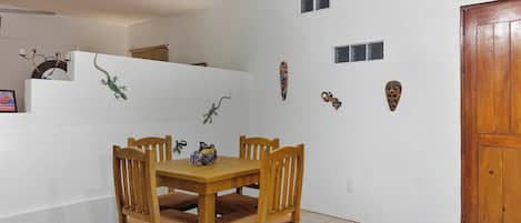 Un coin repas avec une table et des chaises en bois, un mur blanc orné de masques décoratifs et une porte en bois.