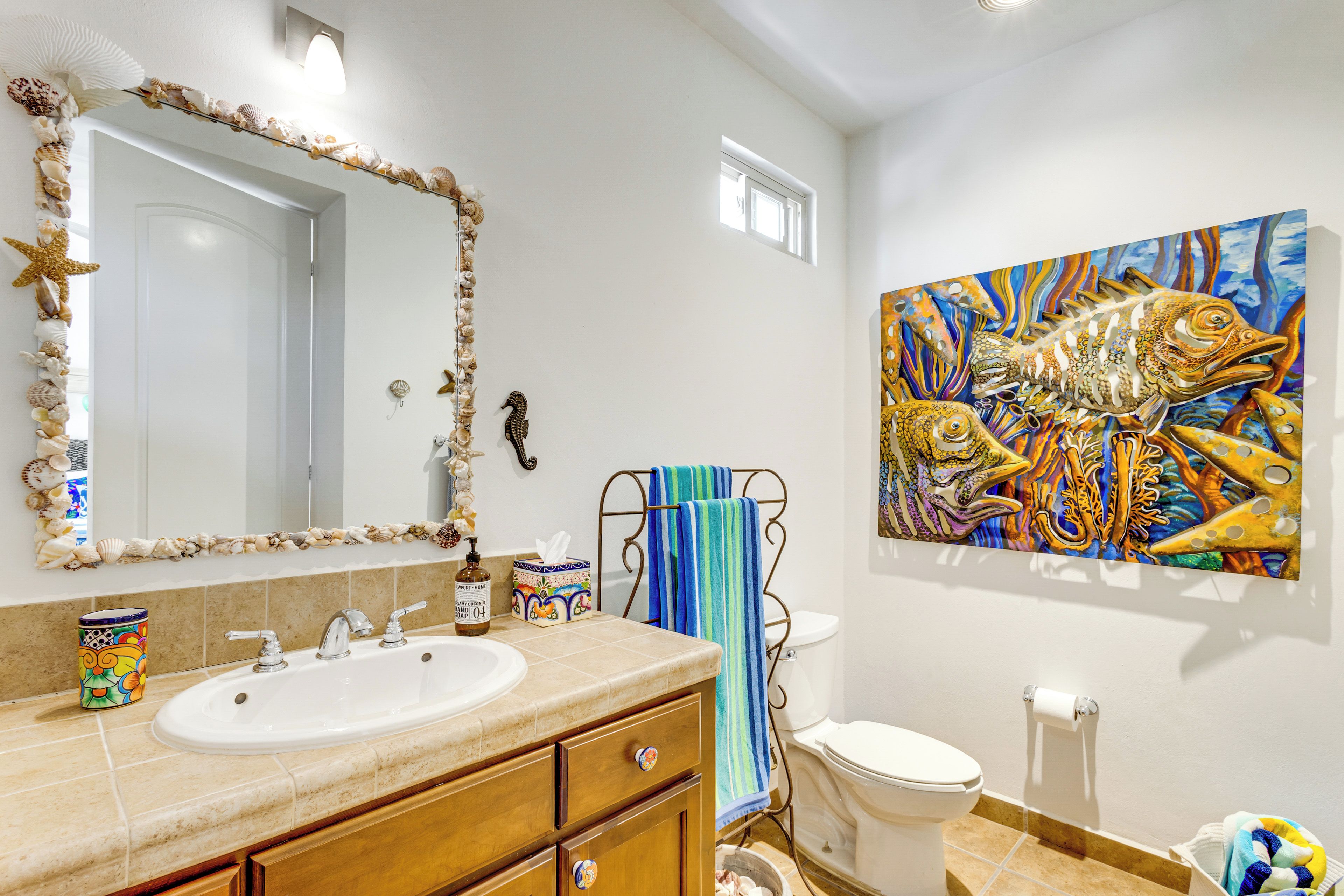 A bathroom with a large mirror, a sink, a toilet, and a colorful fish painting on the wall.