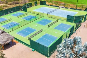 A tennis court complex with multiple courts, surrounded by green fencing and a thatched-roof structure. - Paraiso del Mar Casita: Walk to Beach & Pool! (La Paz)