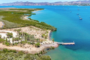Uma área costeira com um cais, barcos e uma praia com palmeiras.