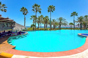 A swimming pool with a curved edge, surrounded by palm trees and a thatched-roof structure.