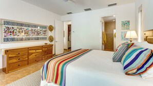 A bedroom with a bed, a wooden dresser, a ceiling fan, and a door leading to another room.