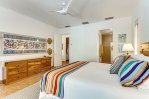 A bedroom with a bed, a wooden dresser, a ceiling fan, and a door leading to another room.