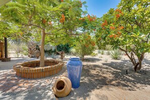 Un jardín con un macetero de ladrillo, una maceta azul grande y diversas plantas.