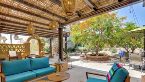 An outdoor seating area with a woven ceiling, a blue sofa, wooden chairs, and a small table.