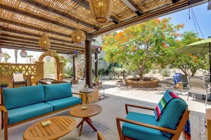 An outdoor seating area with a woven ceiling, a blue sofa, wooden chairs, and a small table.