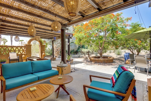 An outdoor seating area with a woven ceiling, a blue sofa, wooden chairs, and a small table.