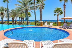 A swimming pool with lounge chairs and palm trees, overlooking a body of water.