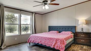 A bedroom with a bed, a ceiling fan, a nightstand, a lamp, and a window with curtains.