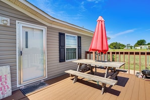 Um deck de madeira com mesa de piquenique e um guarda-sol vermelho, uma porta de correr com vidro e uma caixa de correio.