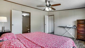 Un dormitorio con cama, ventilador de techo, escritorio con silla y cómoda.