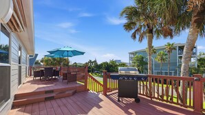 A wooden deck with outdoor furniture, a grill, and a view of a residential area with palm trees and a building. - Walk to the Beach! St. Augustine Group Retreat (St. Augustine)