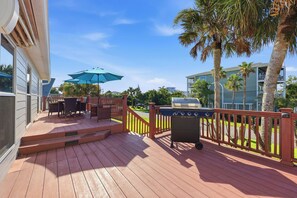 A wooden deck with outdoor furniture, a grill, and a view of a residential area with palm trees and a building. - Walk to the Beach! St. Augustine Group Retreat (St. Augustine)