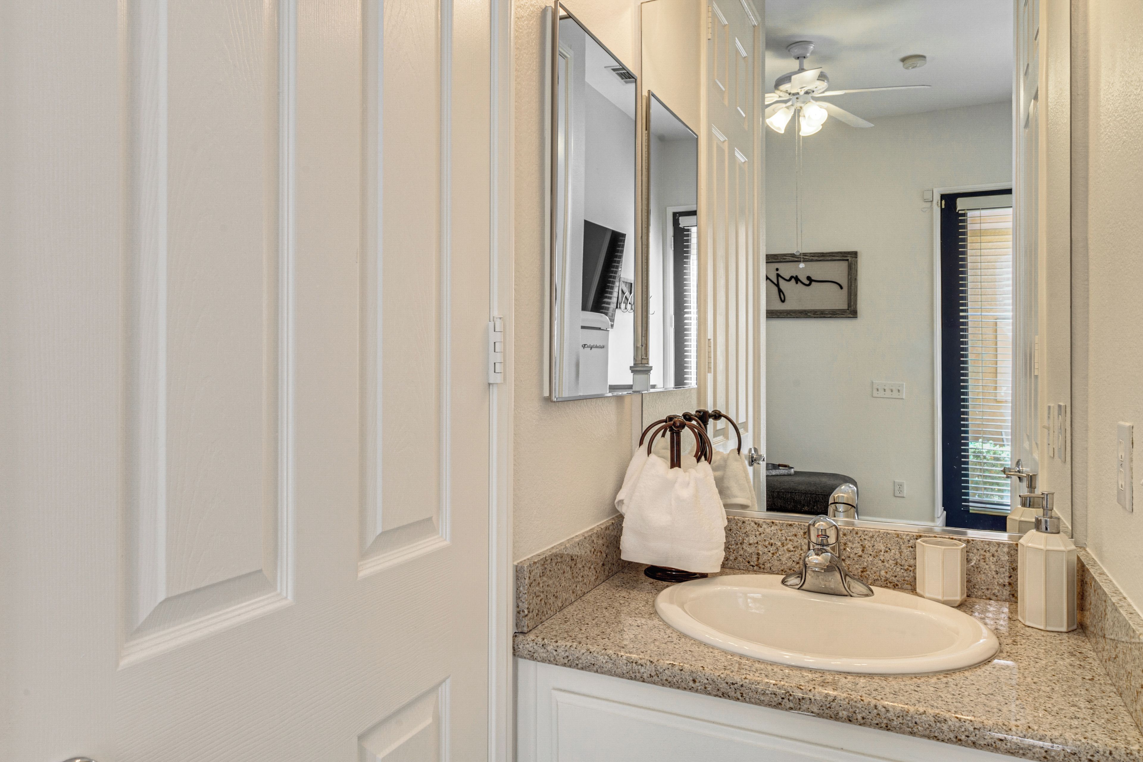 A bathroom with a white sink, a mirror, a towel rack, and a ceiling fan.