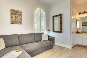 Ein Wohnzimmer mit grauem Sofa, einem Holunderschild an der Wand und einem Fenster mit Jalousien.
