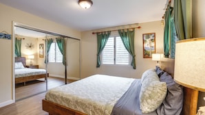 Quarto com uma cama, mesa de cabeceira com abajur, espelho e janela com cortinas.