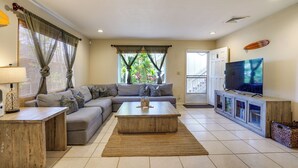 Sala de estar com sofá, mesa de centro, televisão e vista para o verde lá fora.