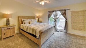 Un dormitorio con una cama de madera, dos mesitas de noche, un ventilador de techo y una ventana con cortinas.