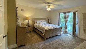 Un dormitorio con cama, lámparas de noche, mesita de noche, cómoda, ventilador de techo y puerta corredera de vidrio al exterior.