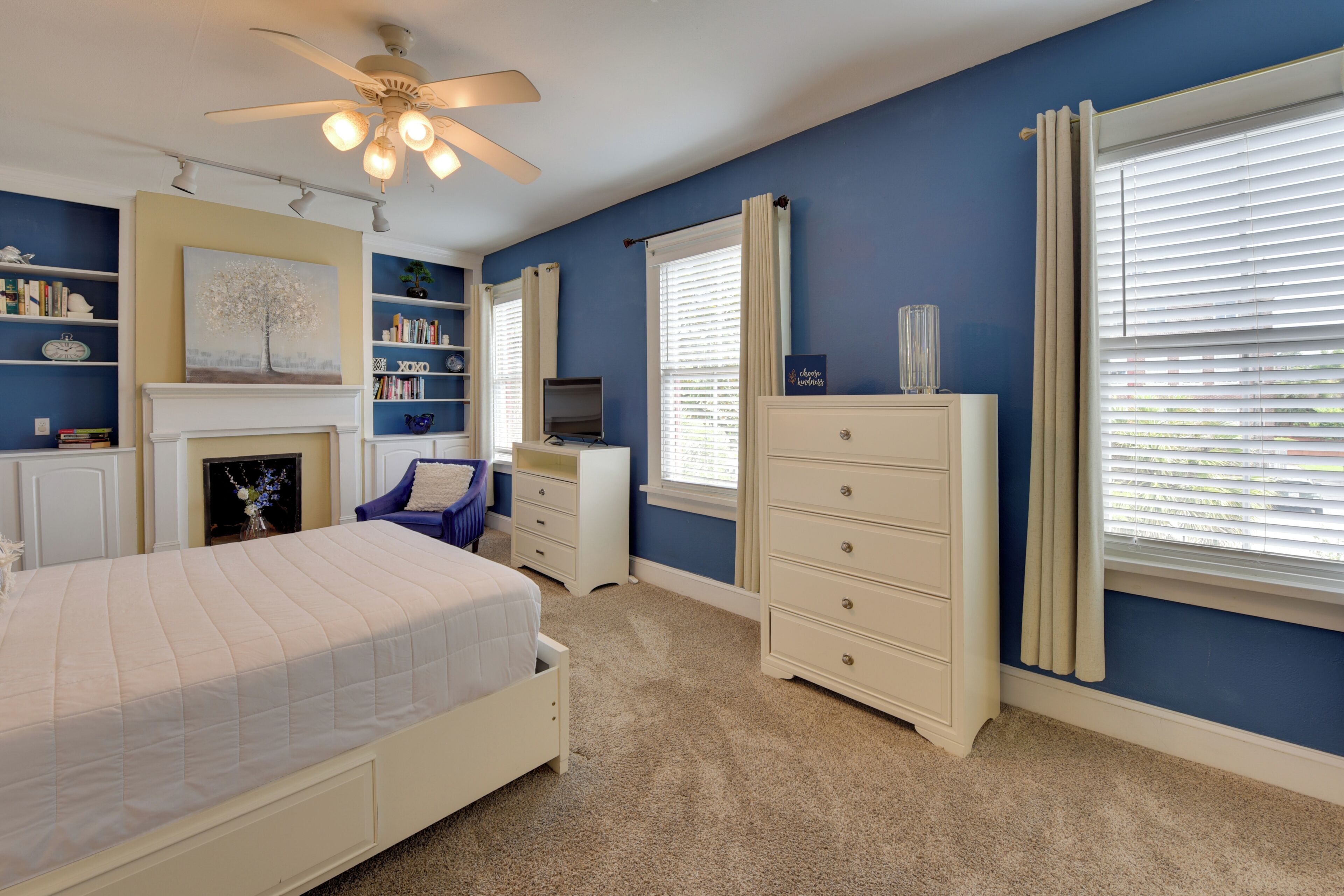 A bedroom with a bed, dresser, TV, bookshelf, and a fireplace.