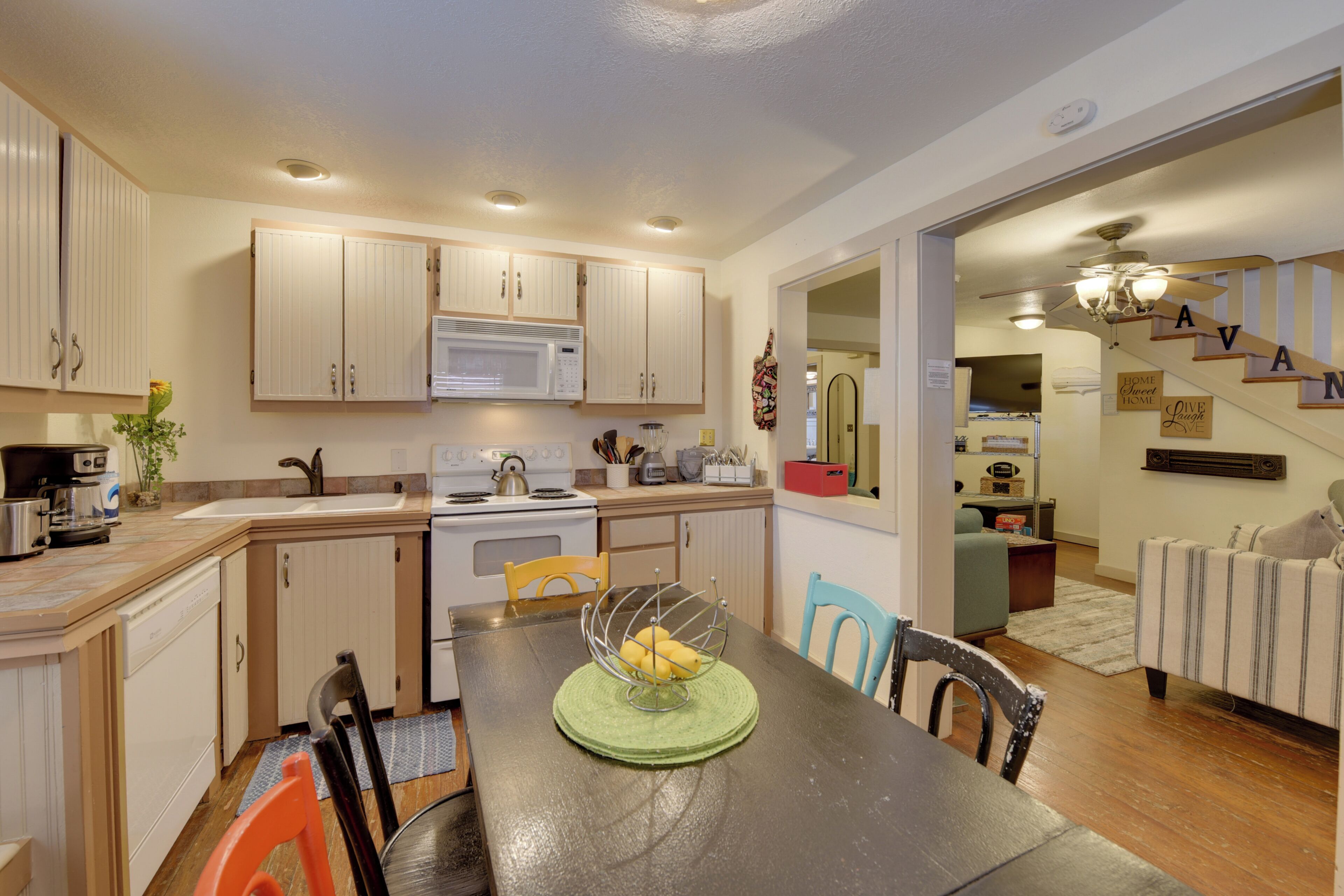 A kitchen with white cabinets, a microwave, stove, and a dining area with a table and chairs.