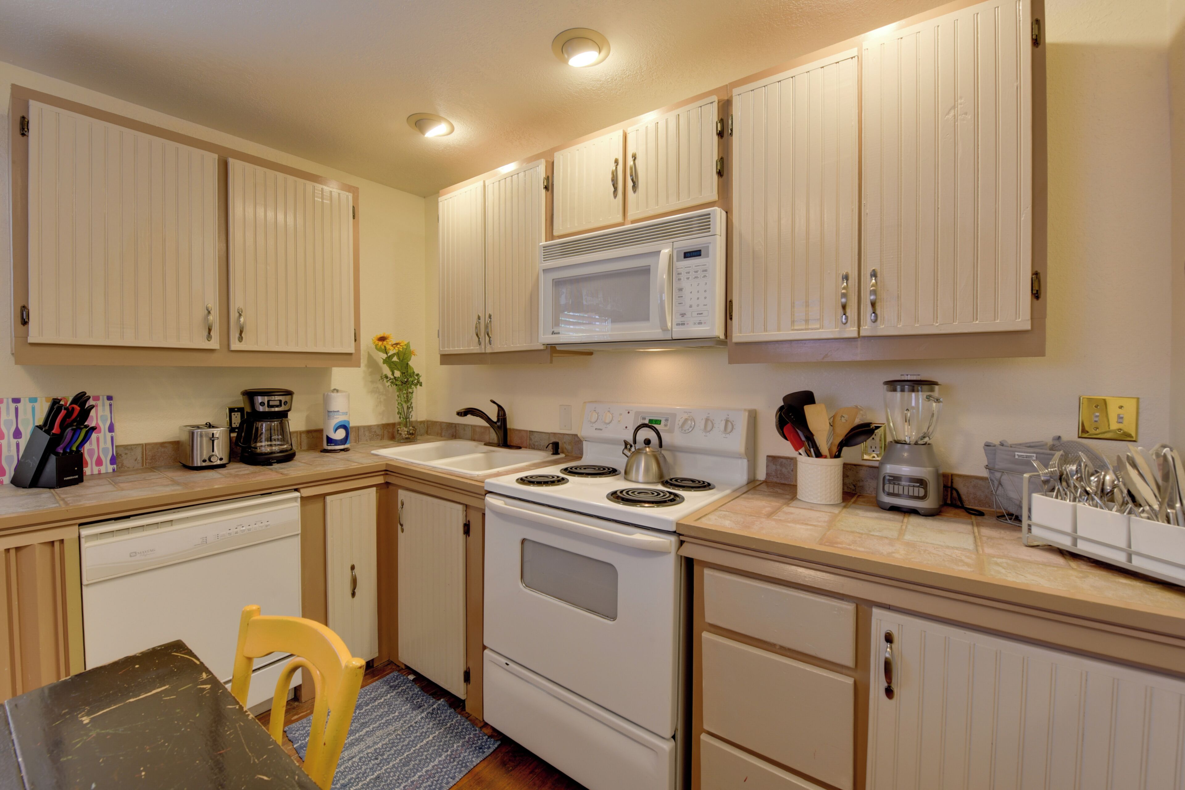 A kitchen with white cabinets, a stove, a microwave, and various appliances.