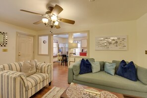 Ein Wohnzimmer mit einem gestreiften Sofa, einem grünen Sofa, einem Deckenventilator und einem Essbereich im Hintergrund.