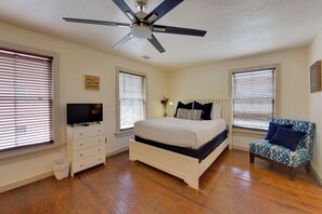 A bedroom with a bed, a television, a ceiling fan, and a window with blinds. - Charming 1870s Carriage House in Historic Downtown (Savannah)