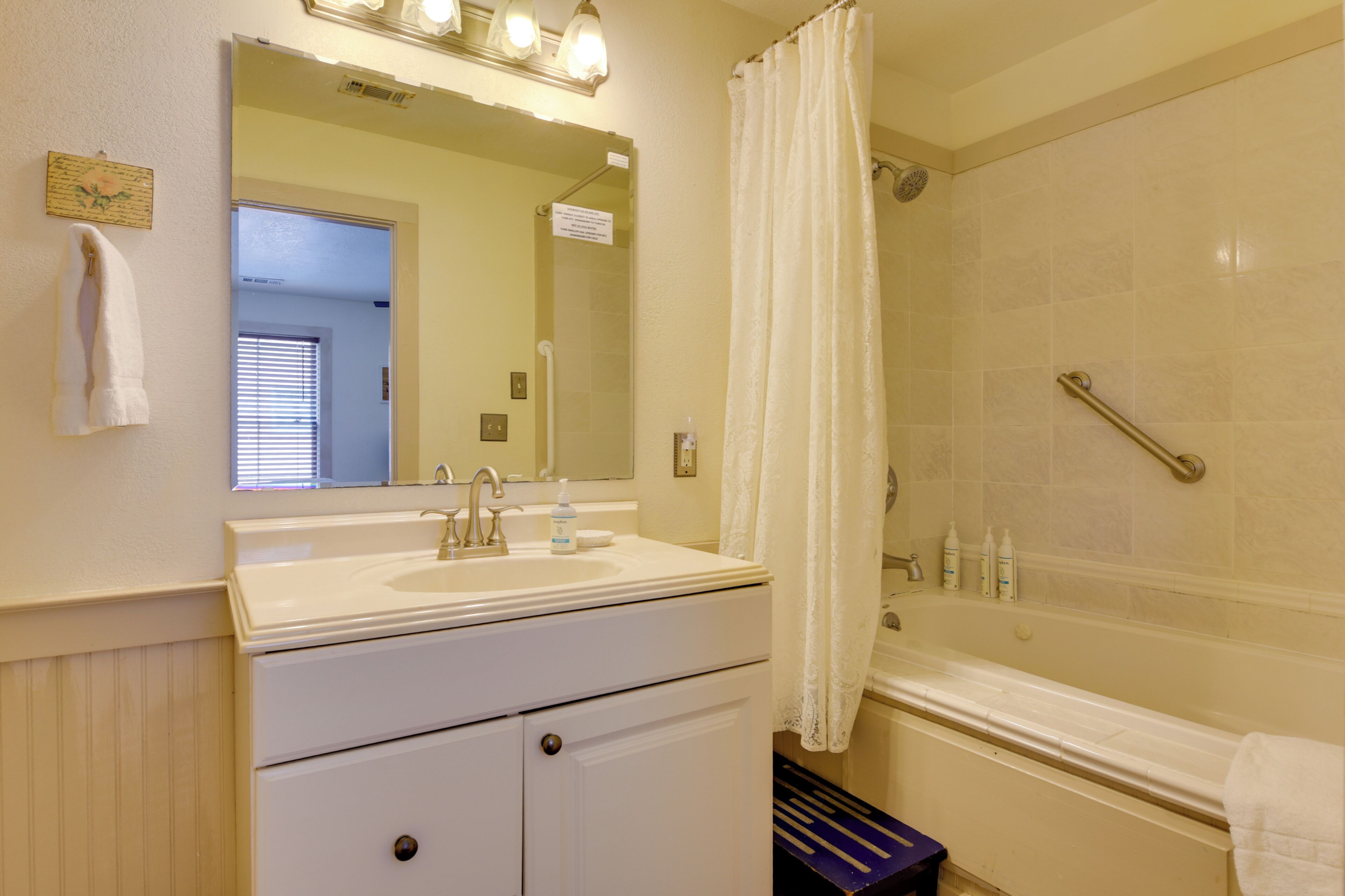 A bathroom with a sink, mirror, shower, and a towel rack.