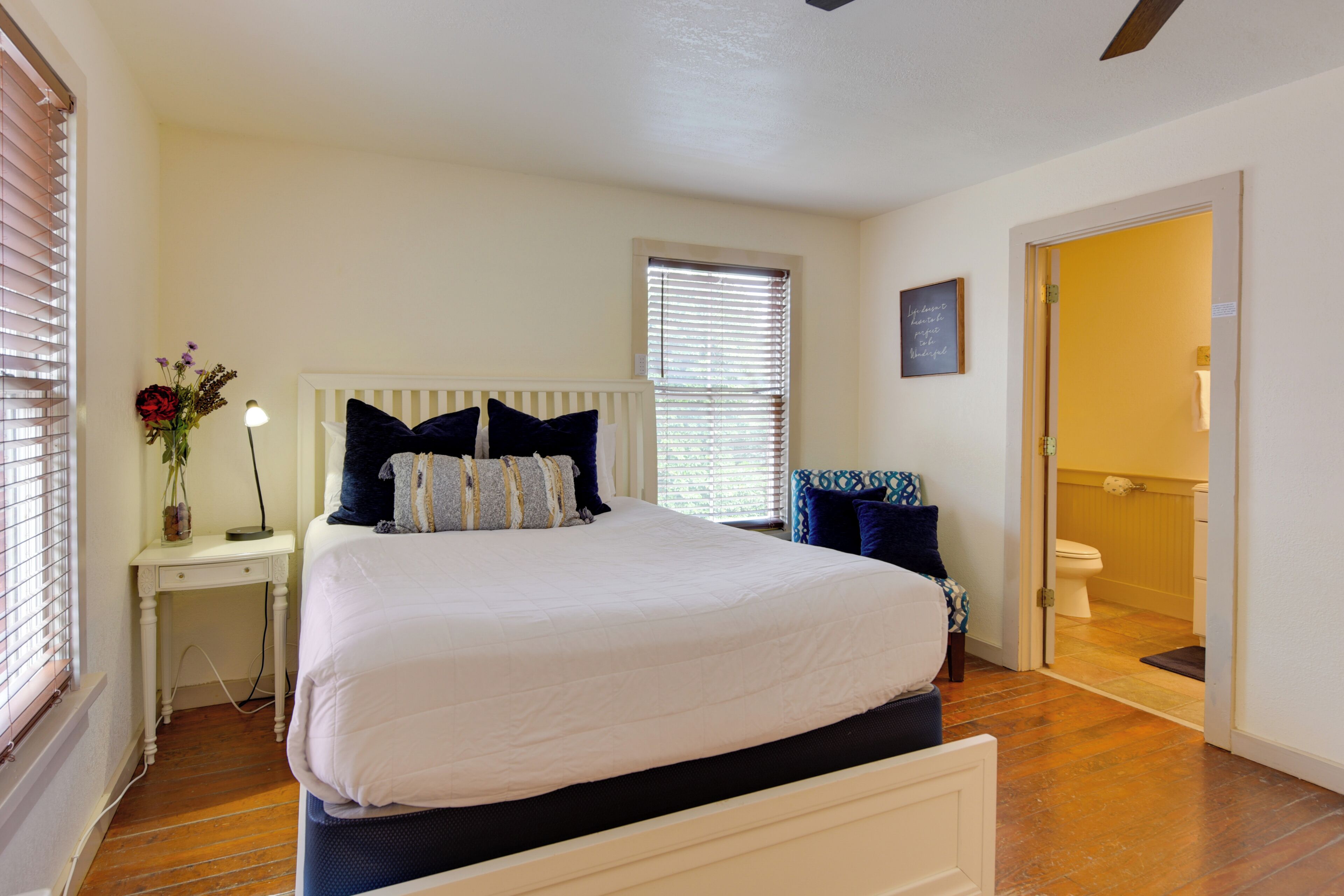 A bedroom with a bed, bedside table, lamp, and a view of the bathroom.