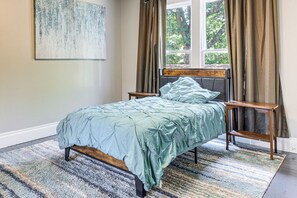 Ein Schlafzimmer mit Bett, Fenster, Vorhängen, einem Gemälde und einem Teppich.