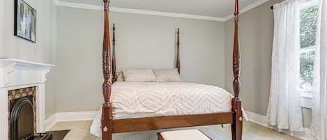 A four-poster bed in a room with a fireplace, a window with curtains, and a ceiling fan.