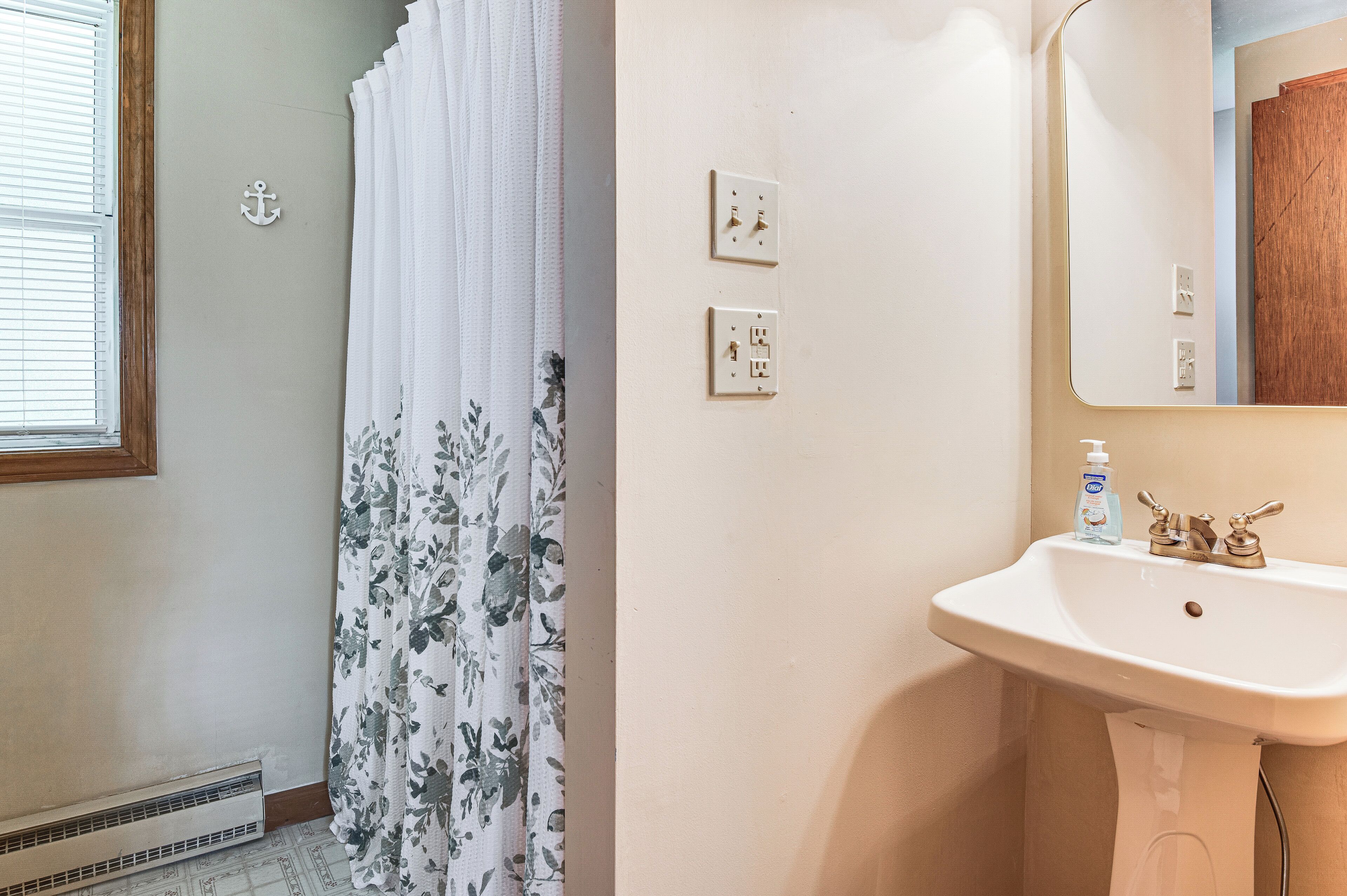 Un baño con lavamanos blanco, espejo y cortina de ducha estampada con motivos florales.
