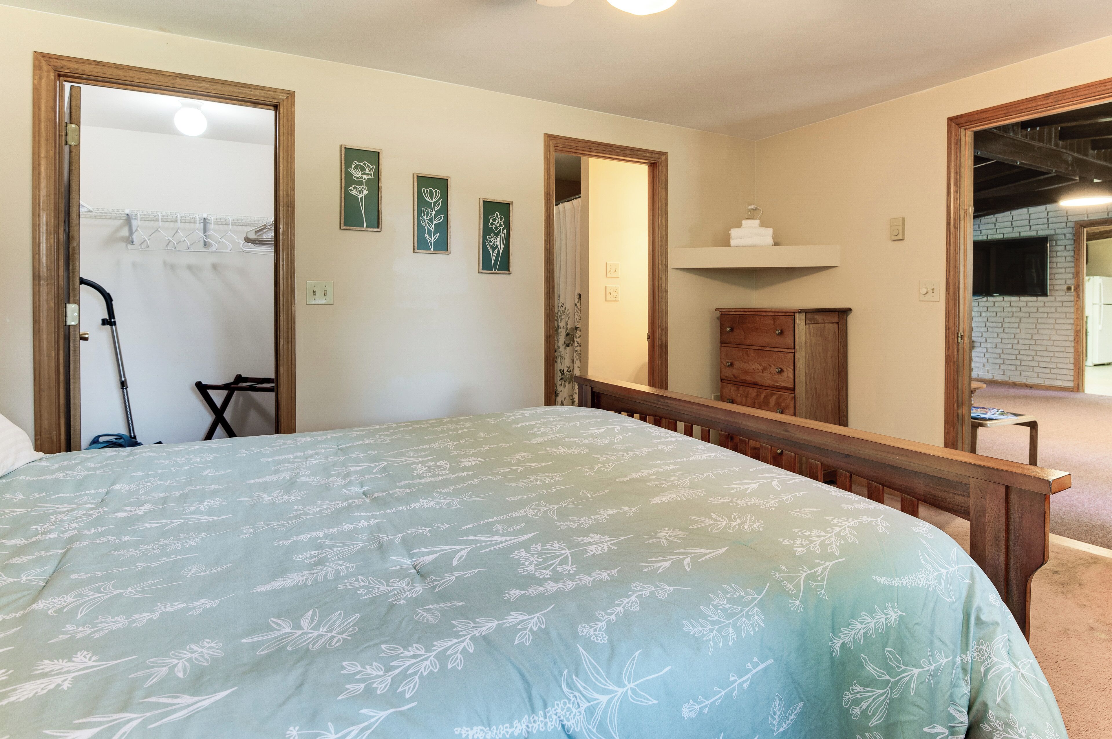 A bedroom with a bed, a wooden dresser, a mirror, and a door leading to a bathroom.