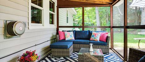 A covered porch with a blue sofa, wicker chairs, a patterned rug, and a flower pot.