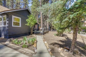 Une cabane en rondins dotée d’une terrasse, entourée d’arbres et bordée d’un chemin de gravier.