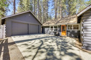A two-car garage attached to a single-story building with a small porch and a wooden door. - Walk to Slopes & Lake! Modern Log Cabin w/ Hot Tub (Big Bear Lake)