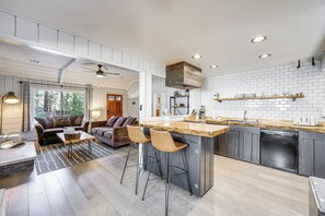A modern kitchen with a central island, bar stools, and a dishwasher. - Walk to Slopes & Lake! Modern Log Cabin w/ Hot Tub (Big Bear Lake)
