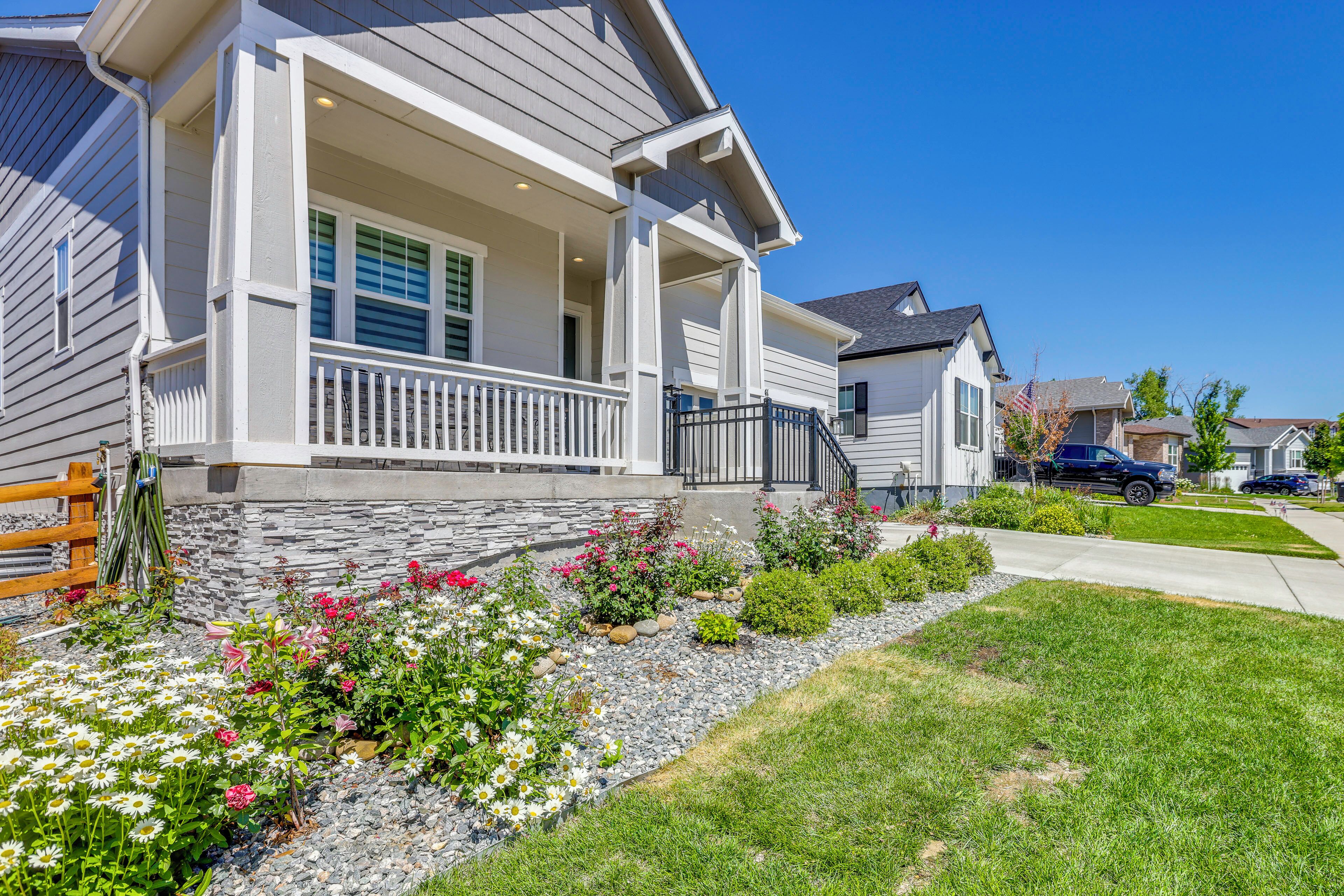 A residential house with a front porch, stone steps, and a well-maintained garden with various flowers.