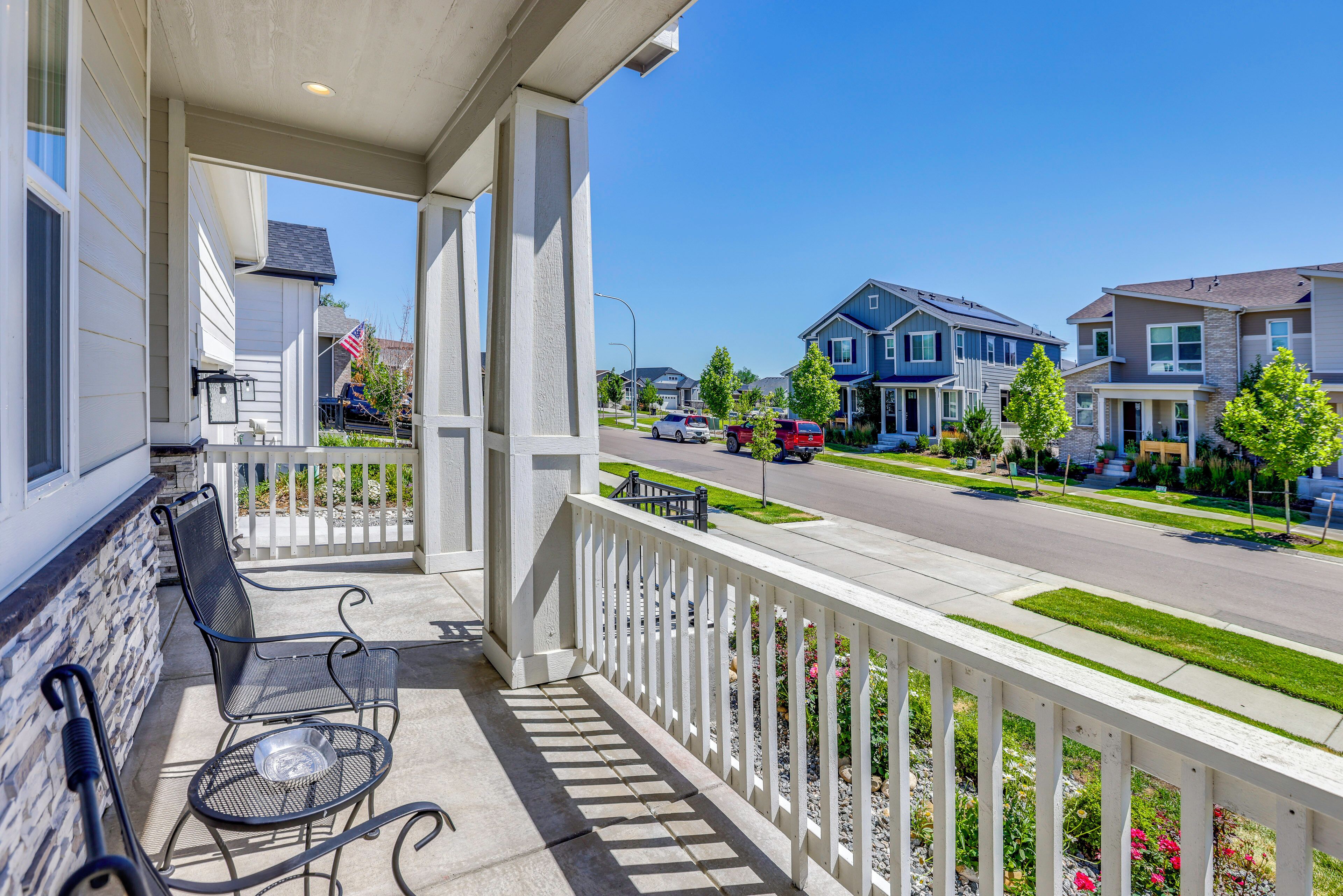 A residential street with houses, a clear sky, and a porch with a bench and a metal table.