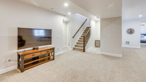 A spacious living room with a flat-screen TV on a wooden stand, a staircase leading to an upper level, and a kitchen area visible through an open doorway. - Great for Families! Arvada Haven w/ Yard & Patio (Arvada)