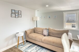 Una sala de estar con un sofá color beige, una mesita auxiliar, una lámpara y un ventanal con persianas.