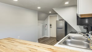 A kitchen with a wooden countertop, stainless steel sink, and a refrigerator.
