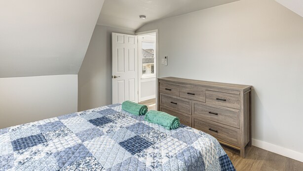 A bedroom with a bed, a wooden dresser, and a door leading to another room.