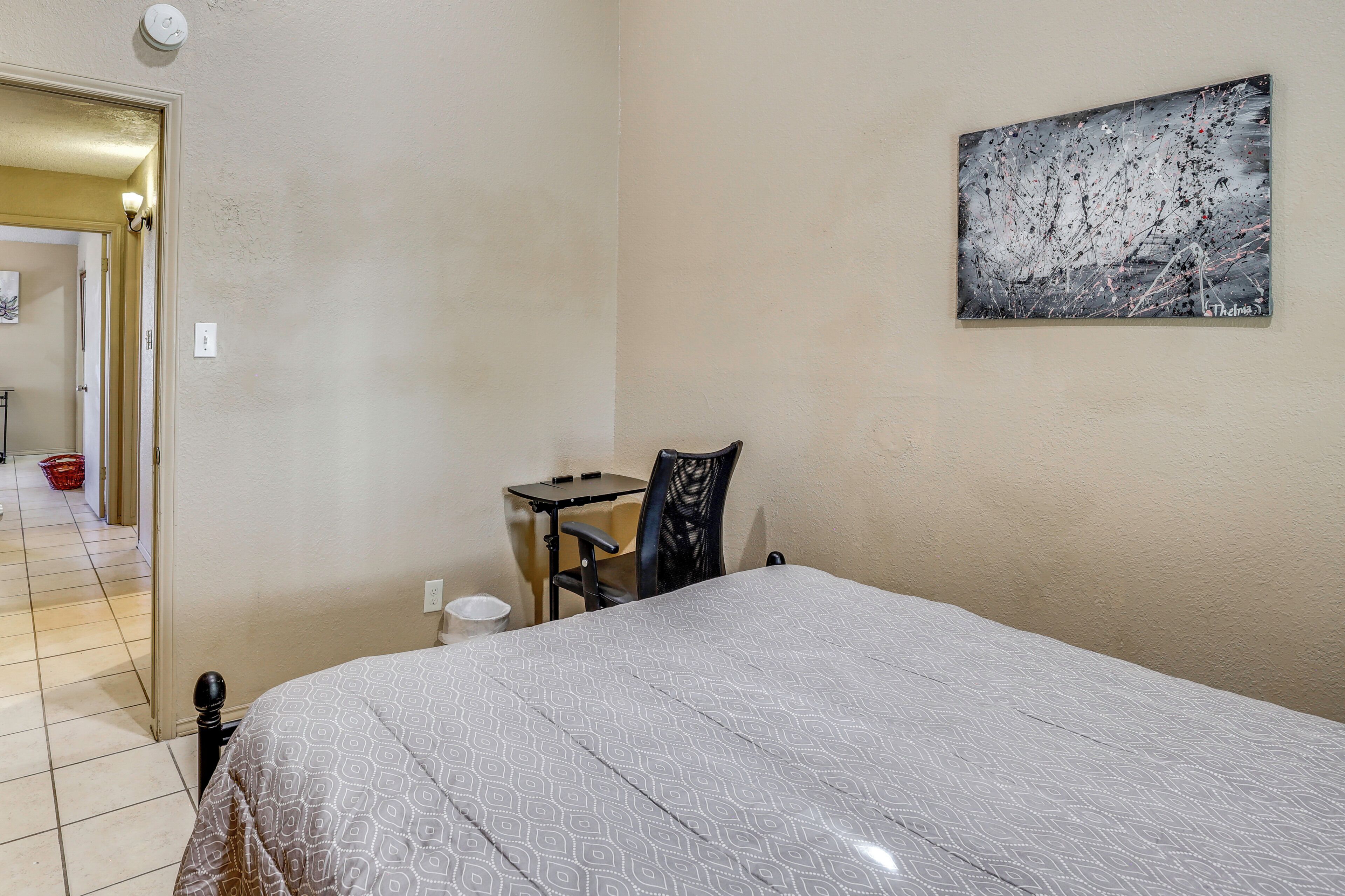 A bedroom with a bed, a desk, a chair, and a painting on the wall.