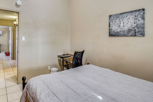 A bedroom with a bed, a desk, a chair, and a painting on the wall.
