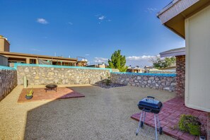 A backyard with a barbecue grill, a fire pit, and a stone wall.