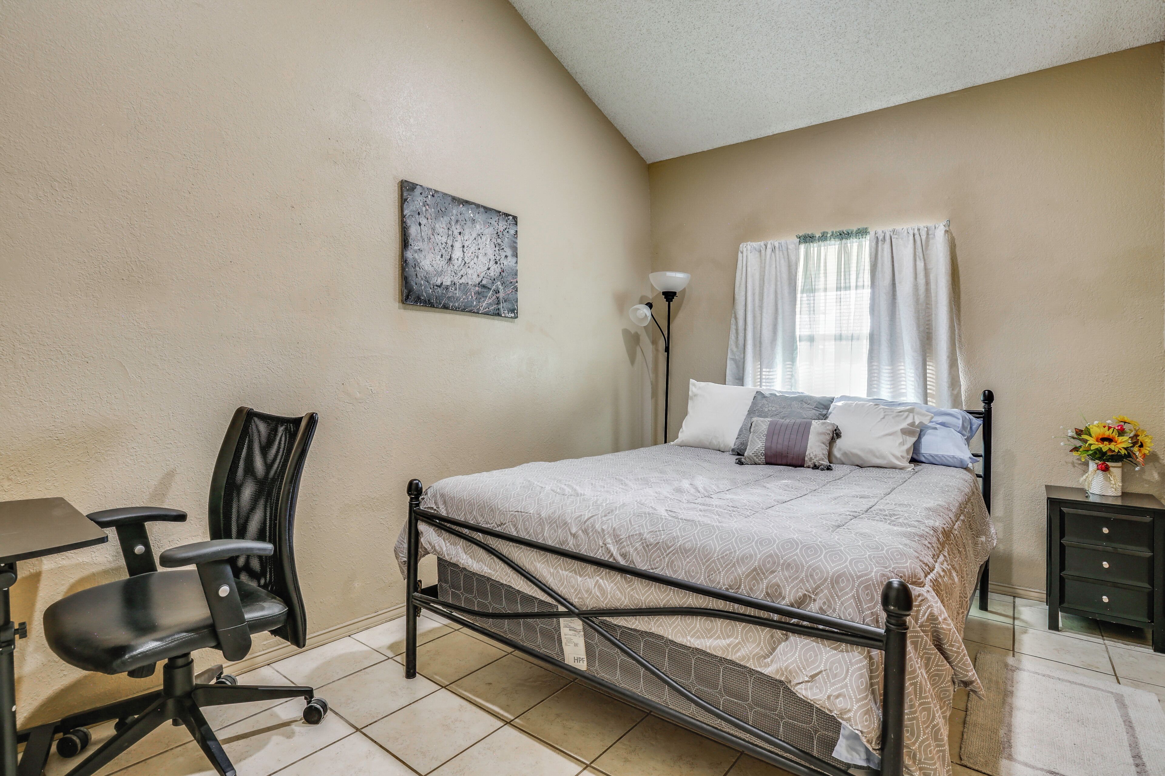 A bedroom with a bed, a desk, a chair, a lamp, and a window with curtains.