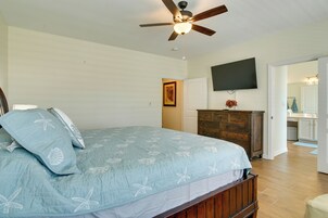 A bedroom with a bed, a ceiling fan, a dresser, a TV, and a bathroom visible through an open door.